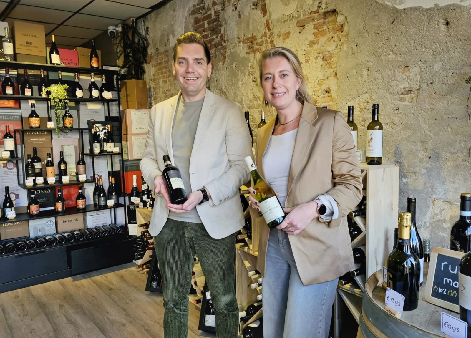 Dennis en Sanne met een fles rood en een fles wit in hun wijnwinkel